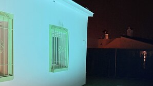 Una piscina con borde iluminado, un edificio blanco con ventana y un área con césped.