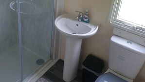 A bathroom with a glass shower enclosure, a white pedestal sink, and a toilet. - 10 Berth Caravan Butlins Skegness Pet Friendly (Skegness)
