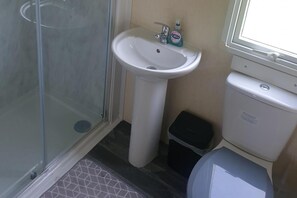 Ein Badezimmer mit Duschkabine aus Glas, einem weißen Waschbecken auf Säule und einer Toilette.