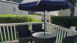 A balcony with wicker chairs and a table, an umbrella, and a view of a house and greenery. - 10 Berth Caravan Butlins Skegness Pet Friendly (Skegness)