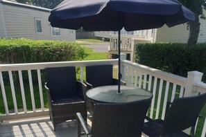Ein Balkon mit Korbstühlen, einem Tisch, einem Sonnenschirm und Blick auf ein Haus und Grünflächen.