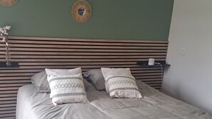 A neatly made bed with a wooden headboard, a vase with flowers, and wall-mounted mirrors. - 140 m2 fenced house (Pouzac)