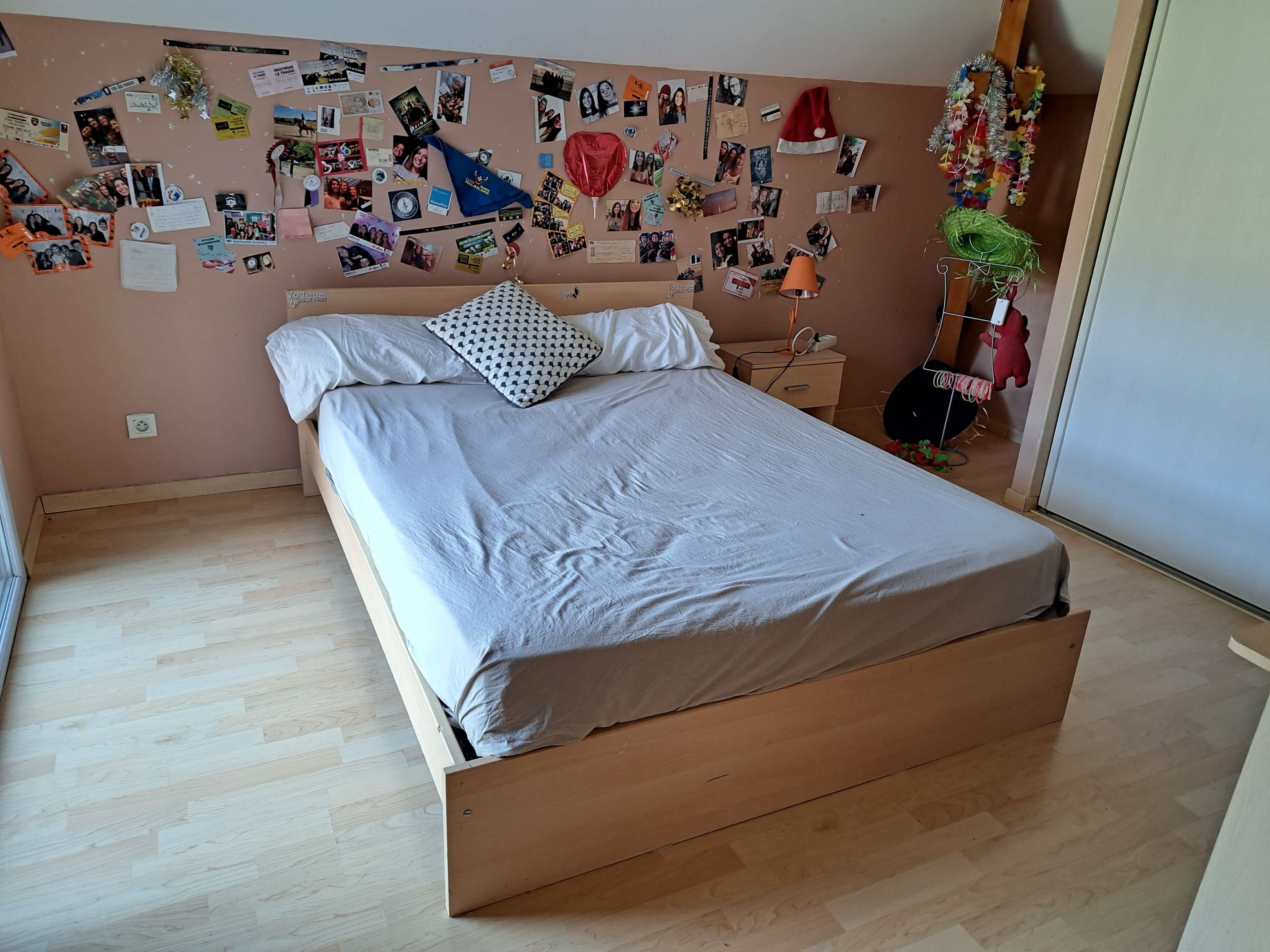 A bedroom with a bed, a wall covered with photos and notes, a guitar, and a plant.