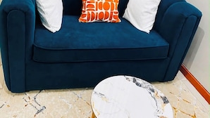 A blue sofa with white and orange cushions, a marble-patterned coffee table with gold legs, and a patterned floor. - Veena Homes | Studio Airbnb in Nairobi (Nairobi)