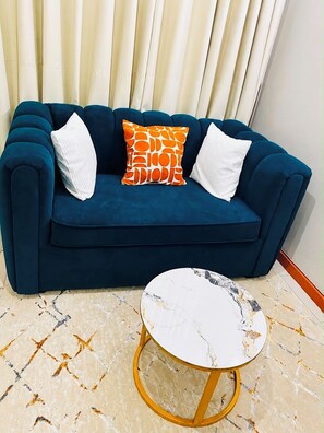A blue sofa with white and orange cushions, a marble-patterned coffee table with gold legs, and a patterned floor. - Veena Homes | Studio Airbnb in Nairobi (Nairobi)