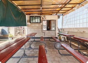 An outdoor seating area with benches and tables, a brick wall, and a window with a poster. - Veena Homes | Studio Airbnb in Nairobi (Nairobi)
