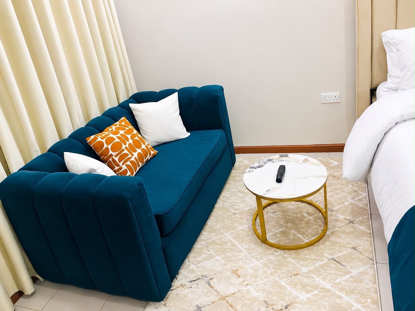 A room with a blue sofa, a white pillow, a patterned pillow, and a small round table with a remote control on it.