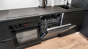A modern kitchen with a built-in dishwasher, oven, and a kettle on the countertop. - Elegant Apartment Near Vitsula River (Łódź)