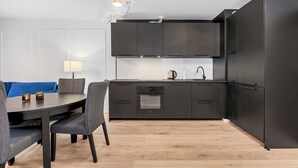 A modern kitchen with dark cabinetry, a built-in oven, and a dining area with a table and chairs. - Elegant Apartment Near Vitsula River (Łódź)