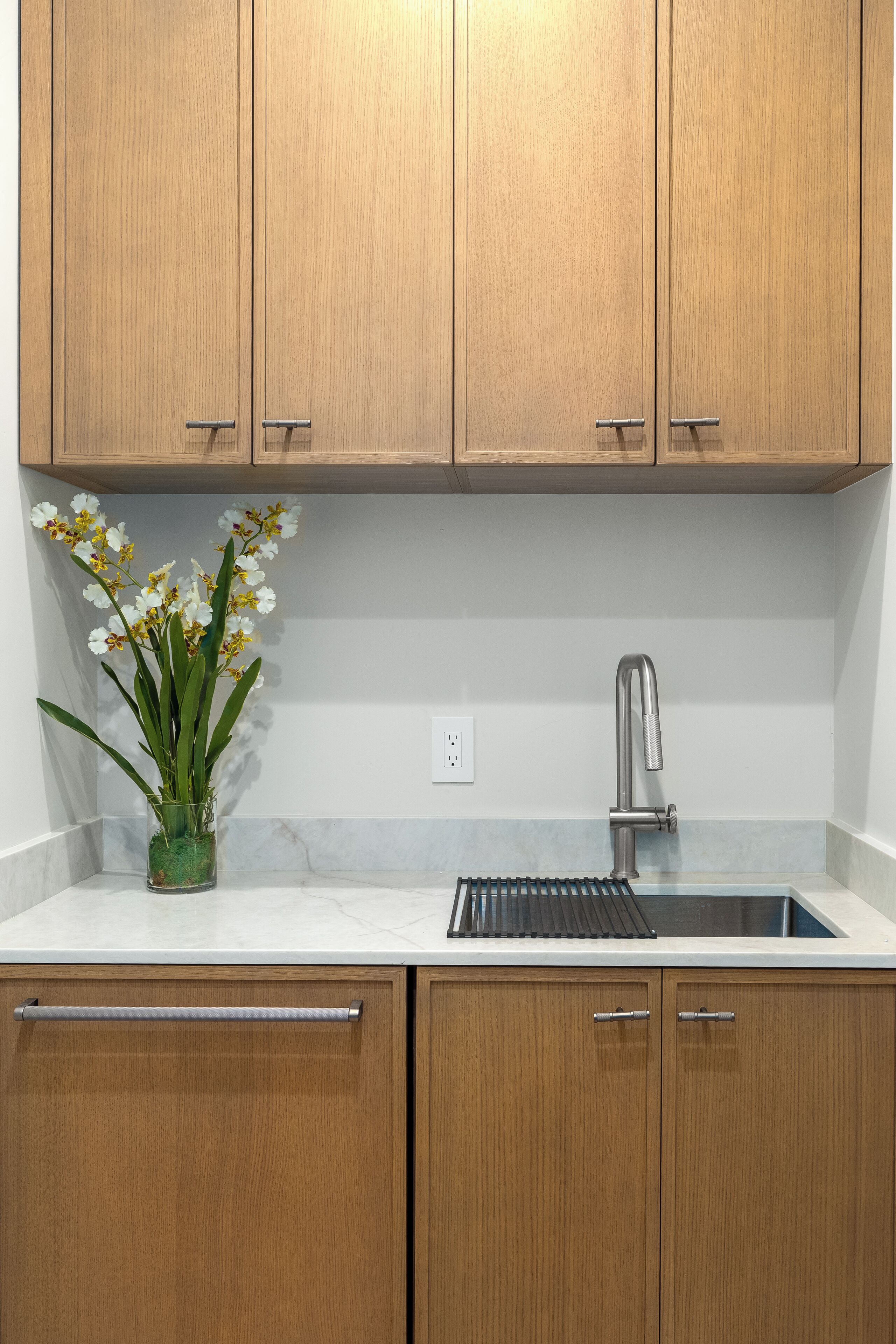 A kitchen with wooden cabinets, a stainless steel sink, and a potted orchid plant.