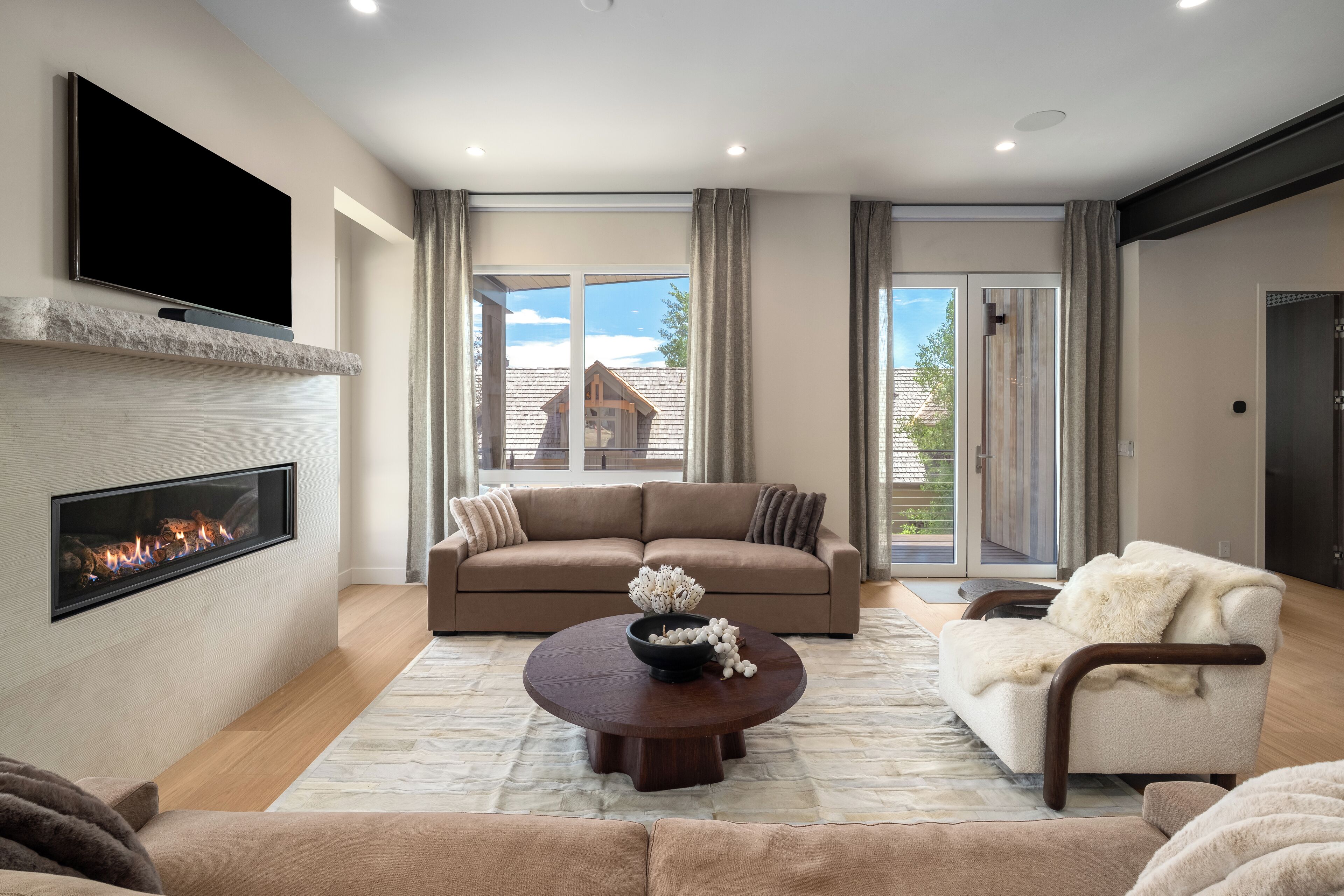 A modern living room with a fireplace, a sofa, a coffee table, and a view of the outside.