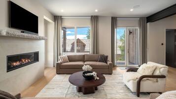 A modern living room with a fireplace, a sofa, a coffee table, and a view of the outside.