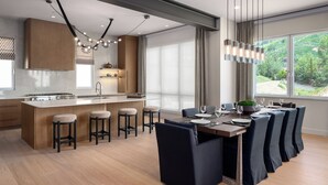Uma cozinha moderna com uma ilha central, banquetas de bar e um espaço de refeições com vista para o exterior.