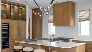 Uma cozinha moderna com uma ilha central, banquetas, forno embutido e exaustor de aço inoxidável.