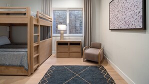 Um quarto com uma cama de solteiro e beliche, uma escrivaninha com abajur, uma cadeira e um quadro na parede.