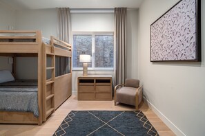 Ein Zimmer mit einem Etagenbett, einem Schreibtisch mit Lampe, einem Stuhl und einem gerahmten Bild an der Wand.