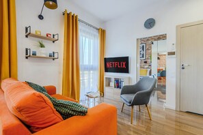 A modern living room with a sofa, armchair, TV, and a bookshelf. - Siedmiogrodzka Flat With Views (Warsaw)