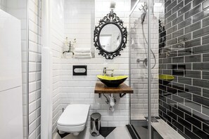 A bathroom with a white toilet, a black and yellow sink, a mirror, and a shower area. - City Center Flat for Families (Warsaw)