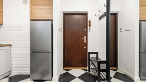 Un pasillo estrecho con suelo a cuadros blanco y negro, una puerta de madera y dos refrigeradores.