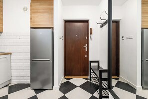 A narrow hallway with a black and white checkered floor, a wooden door, and two refrigerators. - City Center Flat for Families (Warsaw)