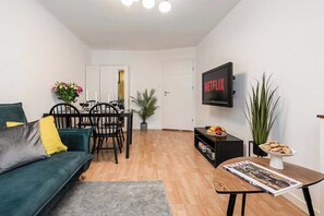 A living room with a sofa, a dining table with chairs, a TV mounted on the wall, and a bookshelf. - City Center Flat for Families (Warsaw)