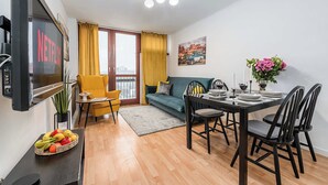 Una sala de estar moderna con televisor, sofá, mesa de comedor y un balcón con cortinas amarillas.