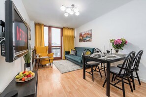 A modern living room with a TV, sofa, dining table, and a balcony with yellow curtains. - City Center Flat for Families (Warsaw)
