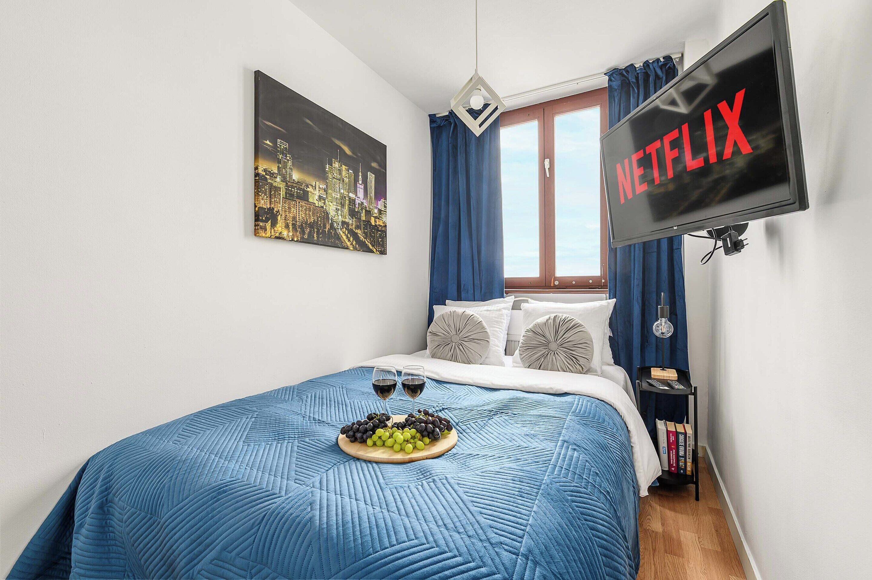 Ein Hotelzimmer mit Bett, Wandfernseher, Fenster mit Vorhängen und einem Wandbild.