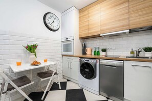 A modern kitchen with white cabinetry, a built-in oven, a washing machine, and a clock on the wall. - City Center Flat for Families (Warsaw)