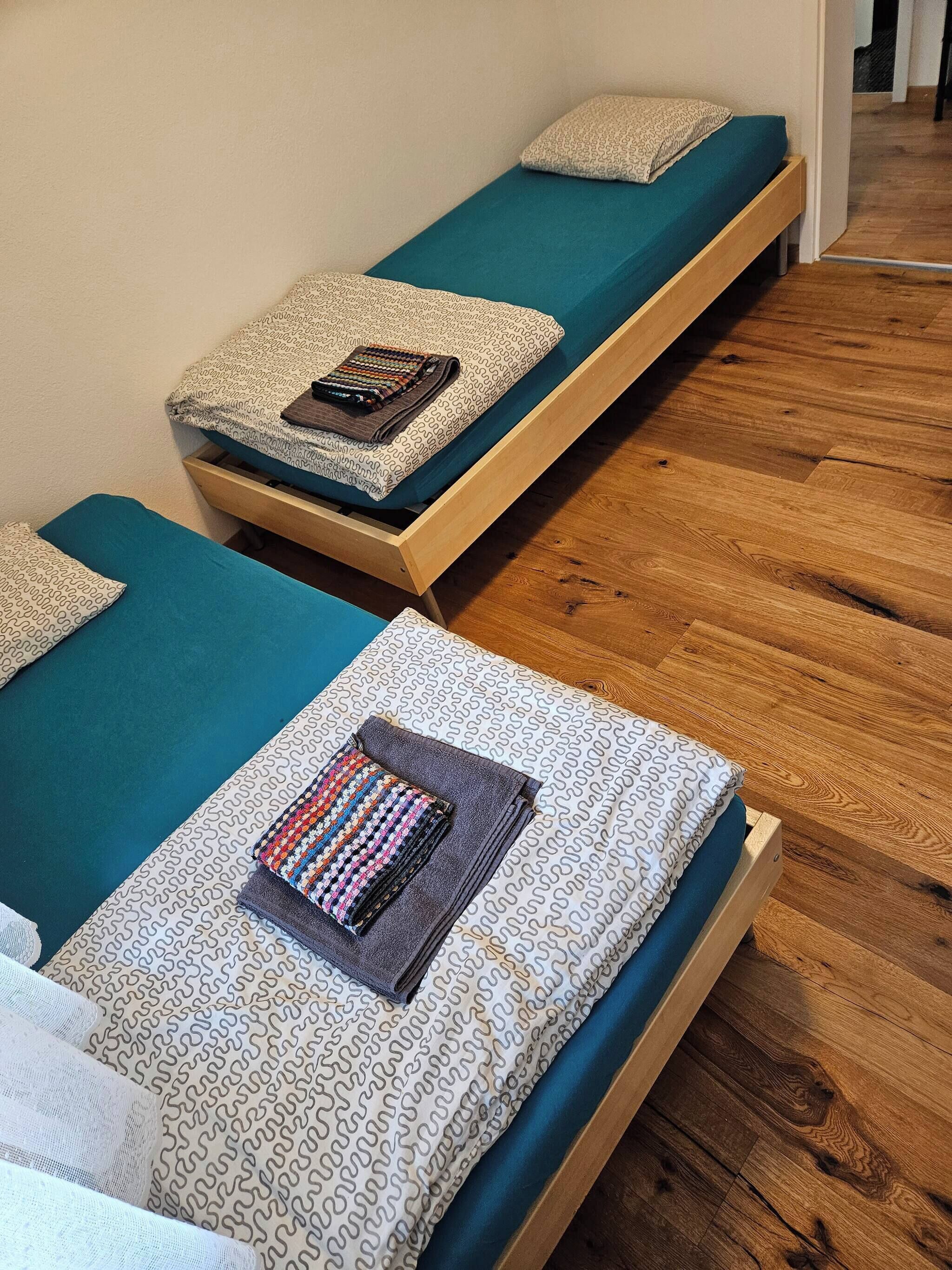 Two single beds with patterned bedding, a wooden floor, and a door in the background.