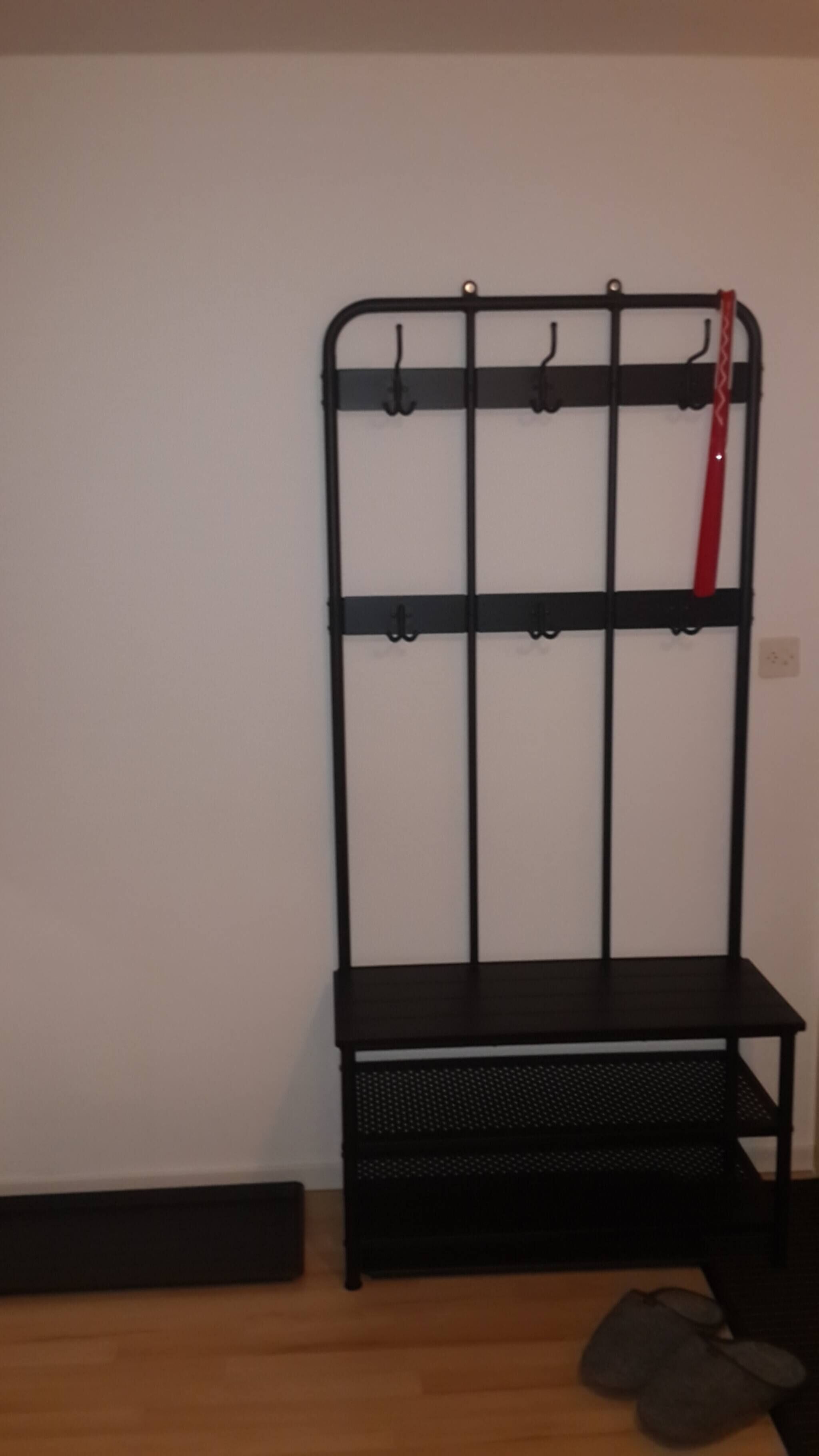 A black metal rack with hooks and a bench against a plain wall.