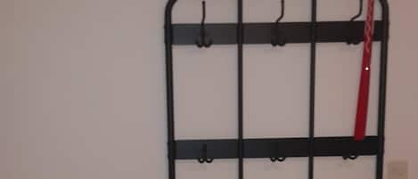 Un présentoir métallique noir, doté de crochets, et un banc adossés à un mur sobre.
