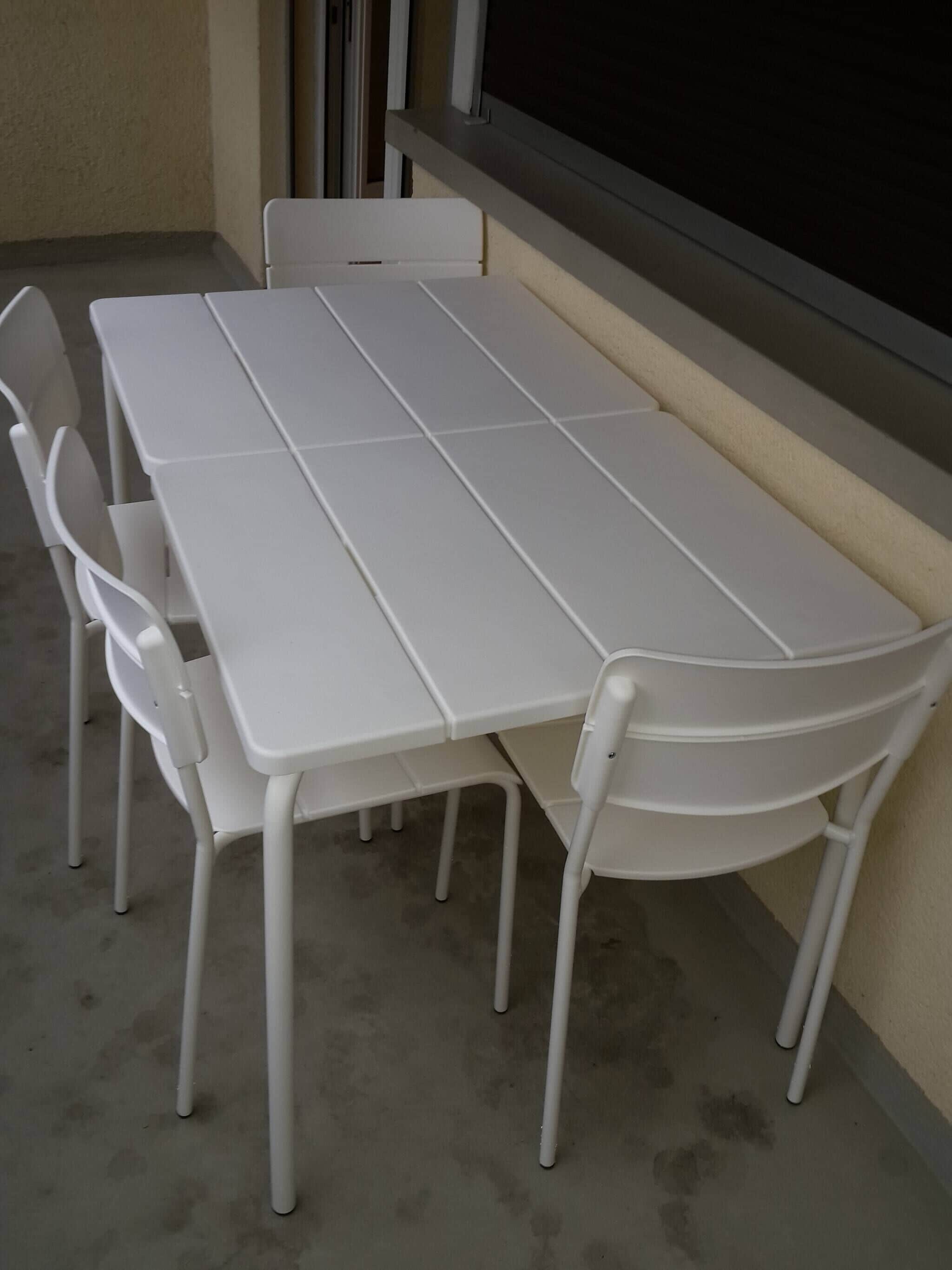 A white table with four chairs, positioned against a wall with a window.