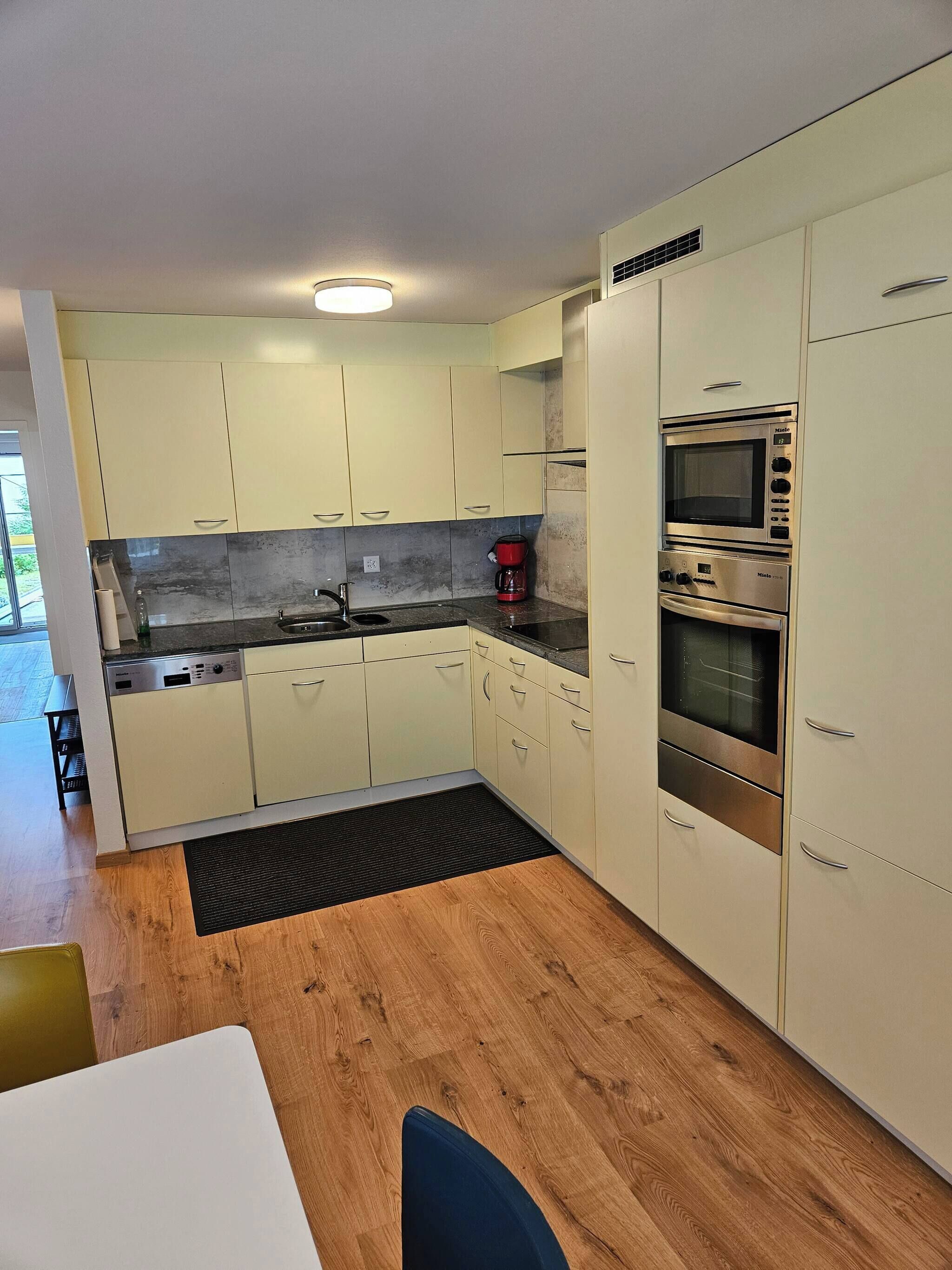 A modern kitchen with light-colored cabinets, a built-in oven, and a coffee maker.