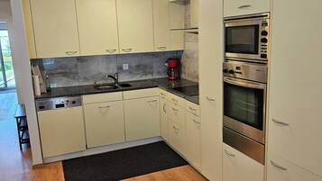 A modern kitchen with light-colored cabinets, a built-in oven, and a coffee maker.