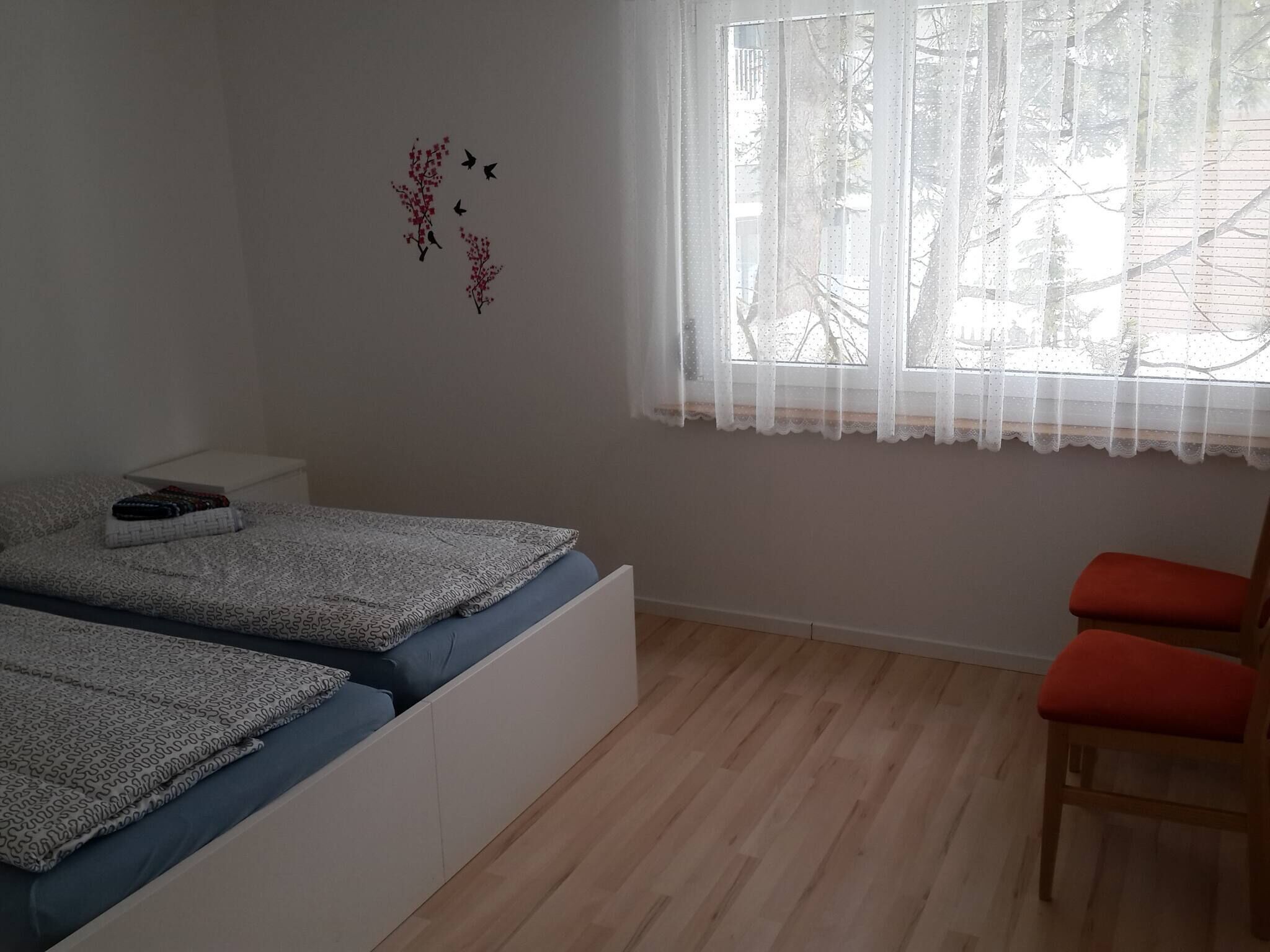 Une chambre à coucher avec un lit, une chaise, une fenêtre donnant sur un paysage agréable et un élément décoratif mural.
