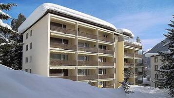 A multi-story hotel with balconies, surrounded by snow-covered trees and mountains.