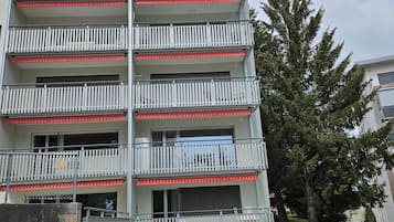A multi-story residential building with balconies, a garage, and a tree in the background.