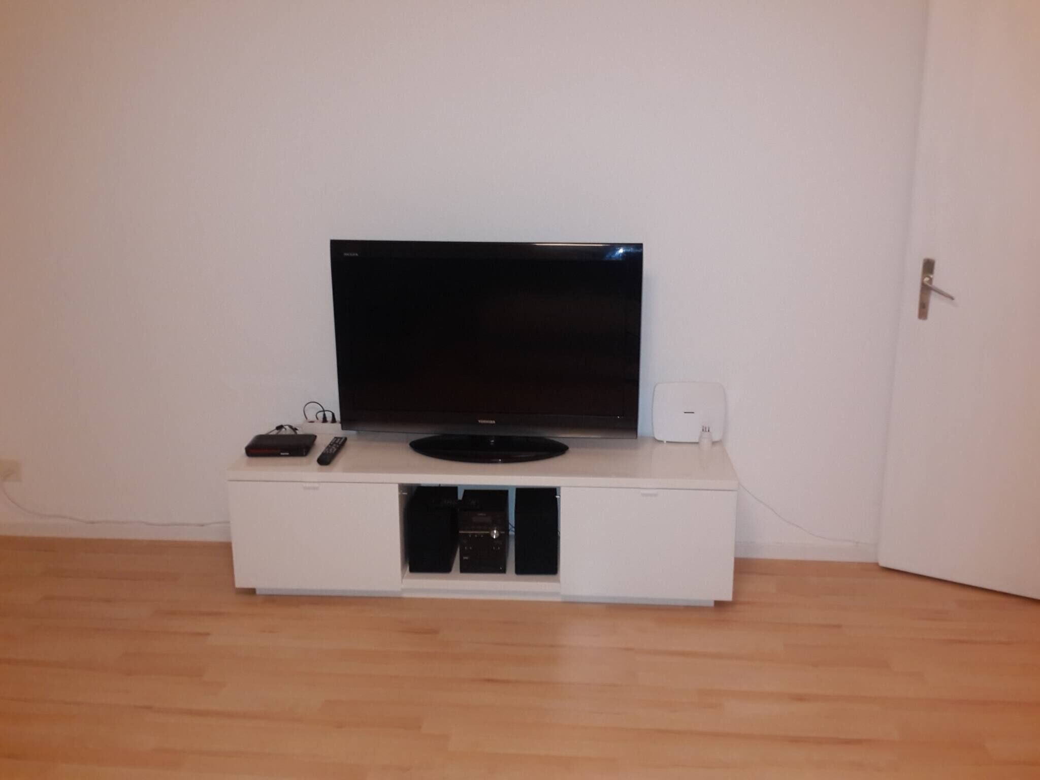 A white entertainment unit with a flat-screen TV, a remote, and a small speaker.