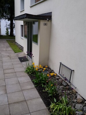 A residential building with a paved walkway, a flower bed with yellow and purple flowers, and a number '9' sign on the wall. - Sesvenna Apartment Davos (Davos)