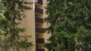 A multi-story building with balconies, surrounded by trees and a grassy area.