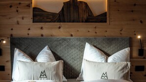 A hotel room with a wooden headboard, two beds with white bedding, and a mountain landscape artwork above the beds.