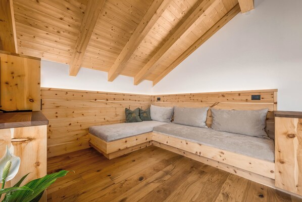 A wooden loft bedroom with a built-in sofa, wooden beams, and a wooden floor.