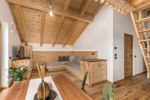 Une pièce de style « loft », avec un plafond en bois, un coin salon intégré, une table à manger et une échelle.