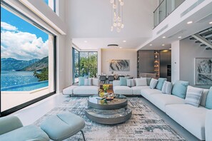 A modern living room with a large window, a sofa, a coffee table, and a dining area. - Ultra Luxury Villa, Breathtaking Bay views (Dobrota)