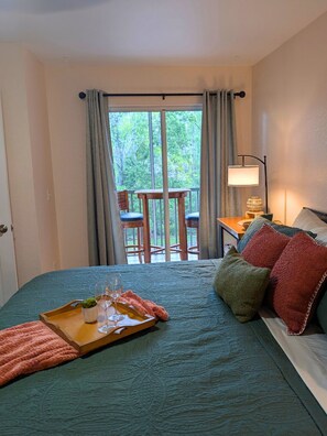 A hotel room with a bed, a small table with a lamp, a view of the outdoors through a window, and a balcony with chairs. - Serengeti Wild and Free - Your Fountains Favorite (Lutz)