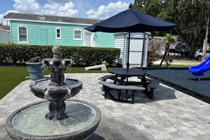 Ein Steinkunstbrunnen, Picknicktische und ein blauer Sonnenschirm in einem Innenhof.