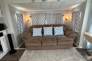 Ein braunes Sofa mit gemusterten Kissen in einem Raum, der mit gemusterten Vorhängen und Wandleuchten ausgestattet ist.