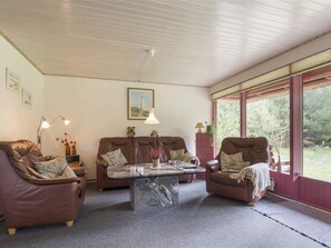 A cozy living room with a brown leather sofa, a matching armchair, and a coffee table. There is a window with a view of greenery outside. - 5 Star Holiday Home in Blavand (Blavand)