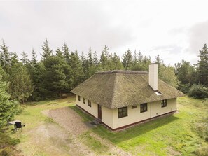 Ein eingeschossiges Haus mit Strohdach, Schornstein und einem kleinen Vorgarten mit Kiesweg zum Eingang.